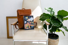 Load image into Gallery viewer, Image of a notebook on a white leather chair with a large planter to the left of the chair.
